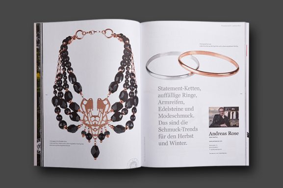 Magazin-Doppelseite mit freigestelltem schwarzem Edelstein-Collier in Roségold sowie glänzenden Armreifen in Silber und Roségold.