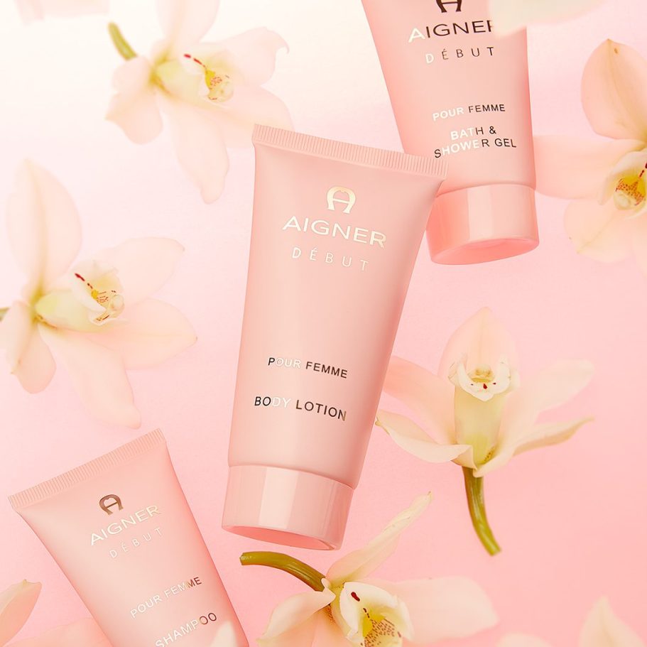 Beauty-Produktfotografie für Aigner Début: Drei roséfarbene Kosmetiktuben mit glänzender Goldprägung, inszeniert zwischen zarten Orchideen