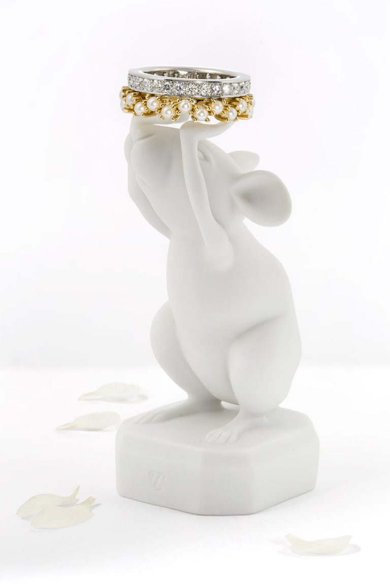 Kreative Schmuck-Inszenierung: Weiße Porzellanfigur hält einen Brillantring und einen goldenen Perlenring zwischen zarten Blütenblättern 