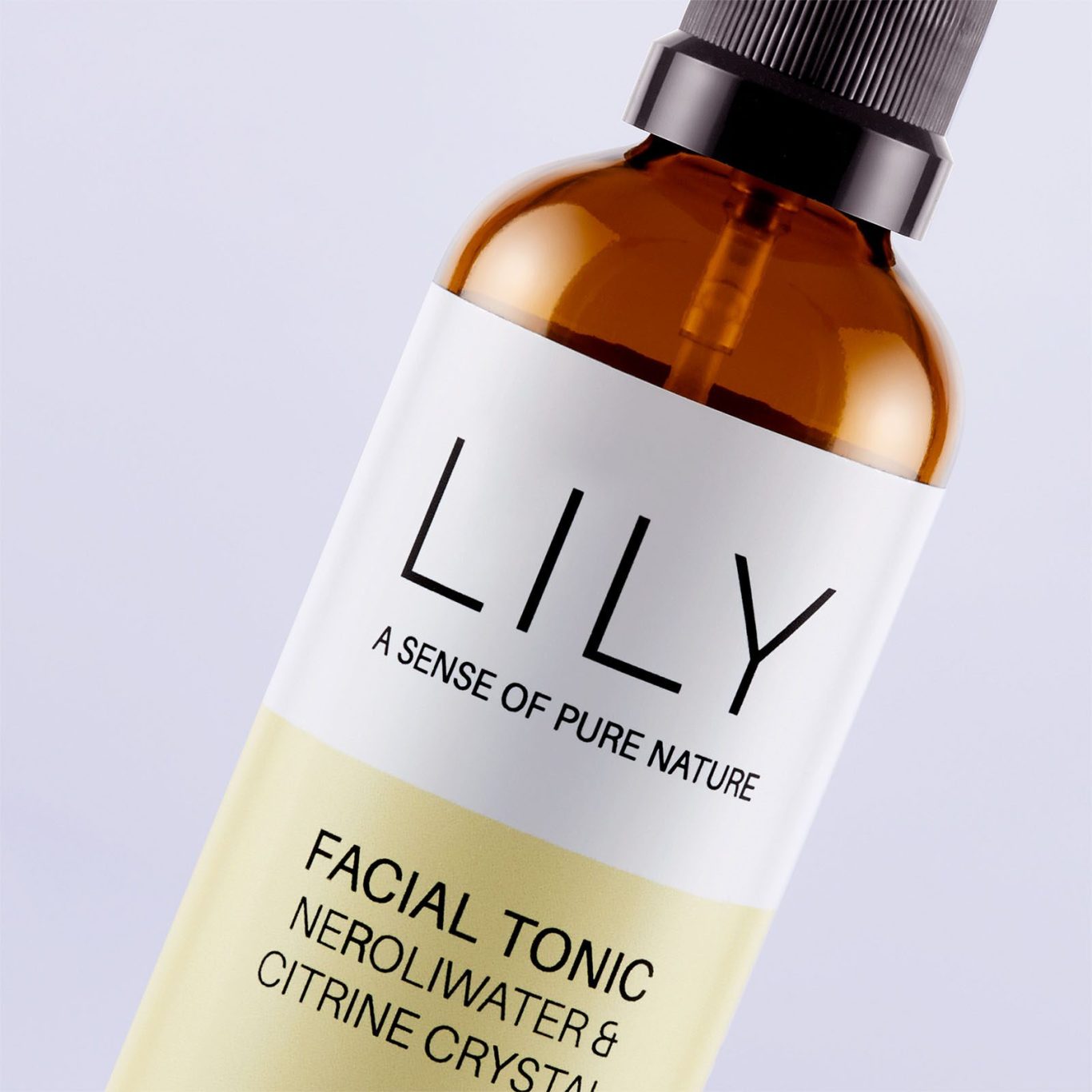 Detailaufnahme eines Naturkosmetik-Braunglasflakons (Lily Facial Tonic) mit warm leuchtender Glas-Transparenz und strukturiertem Papierlabel